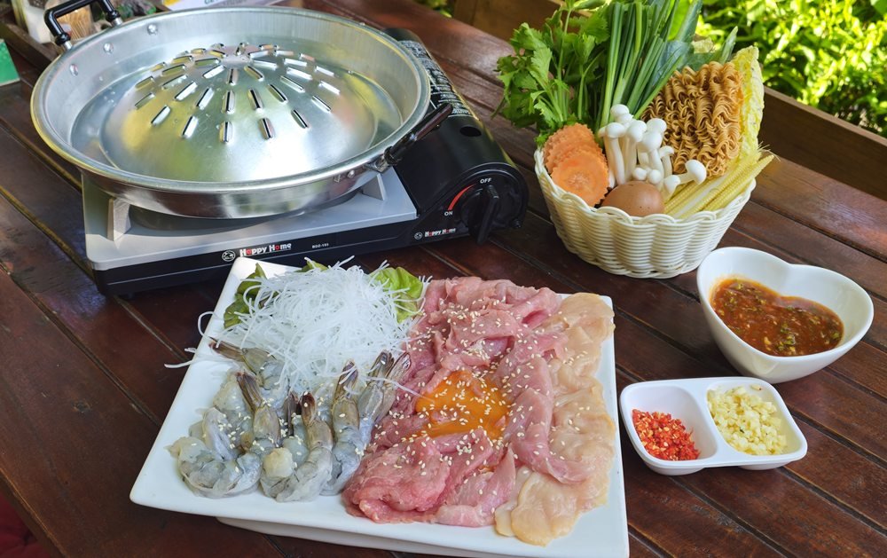 Thai suki hotpot set with prawns, pork and fresh vegetables on a garden table at WonderlanD, Khao Lak